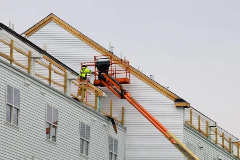 a worker installs panels siding on the facade of the house
